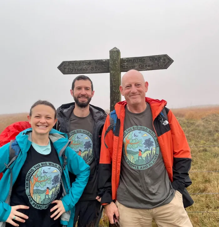 A woman and two men stood in front of a sign post on the Pennine way. The weather is misty.