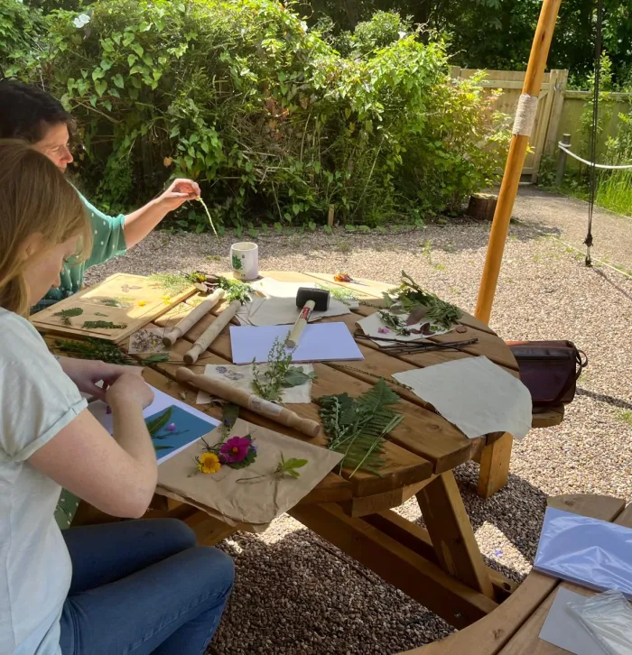 Two people sat outside using leaves and petals to make prints