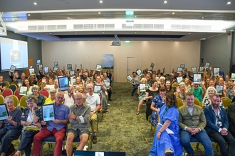 All award winners with their certificates in a crowded conference room.