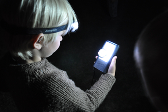 A child in the dark, wearing a head torch and looking at a bat detector