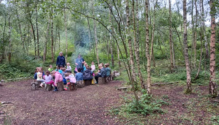 Forest school kids gather round a fire with the leader standing in the middle