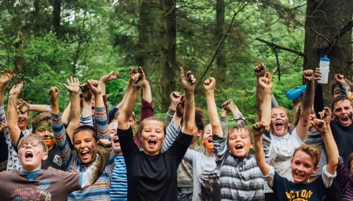 Children with their hands in the air and paint on their faces in a woodland