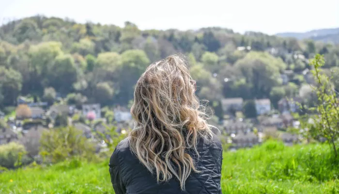 Woman with flowing hair sits with her back to the camera looking out at nature