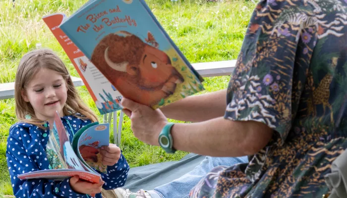 Alice Hemming holding a copy of 'the Bison and the Butterfly', reading to a child also holding a copy of the book.