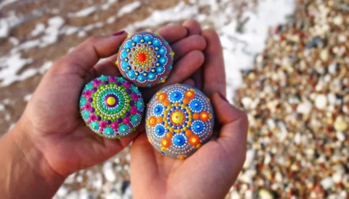 Someone holding three colourfully painted rocks in their hands.