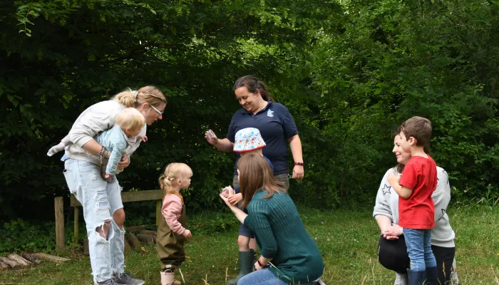 A group of toddlers and adults listening to a Kent Wildlife Trust tutor showing what has been found during a mini-beasting session.