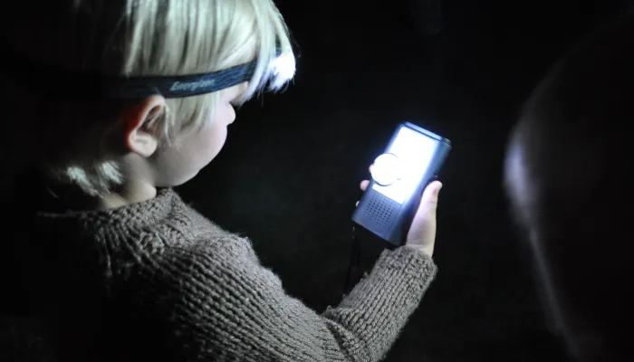 A child wearing a jumper and head torch looking at a bat detector
