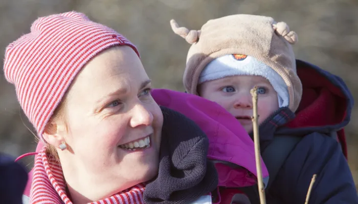 A lady in a hat and scarf carrying a baby in a hat on her back