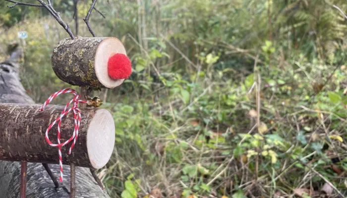 Two pieces of branch joined with twigs to make the shape of a reindeer, with a red pompom nose and ribbon around its neck.