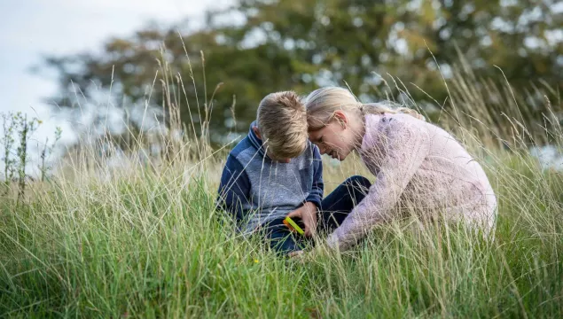 Two children outdoors in long grass using a magnifying glass.