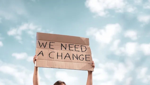 "We need change" written on cardboard and being held up by a climate change protester