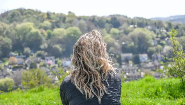 Woman with flowing hair sits with her back to the camera looking out at nature