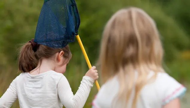 Two children walking away from the camera with a pond dipping net