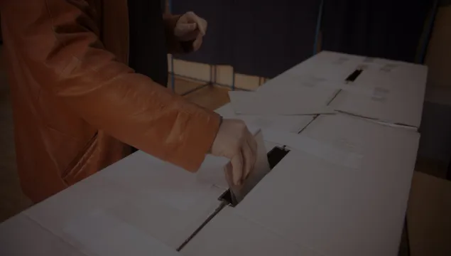 Person in a leather jacket putting a ballot paper into a box