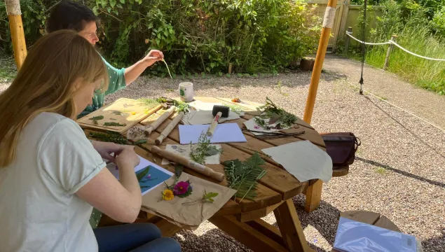 Two people sat outside using leaves and petals to make prints