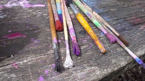 A selection of brushes covered in paint on a wooden bench