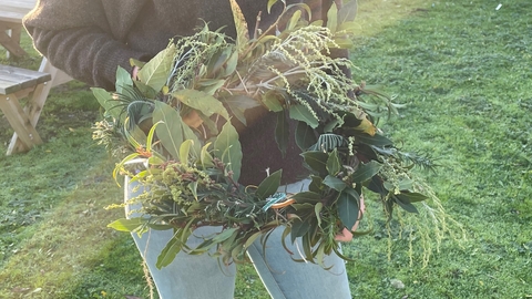 A person holding a festive wreath made from willow and seasonal foliage