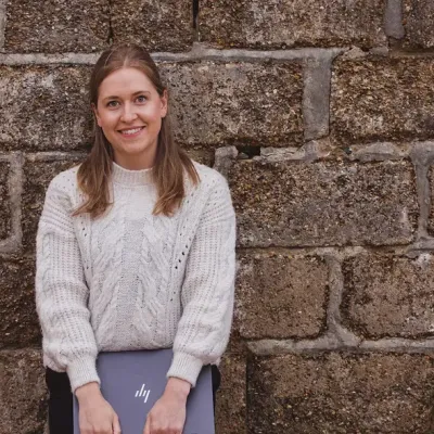 Katie Carr, Business Support Officer at KWT, standing with a laptop in front of a stone wall.