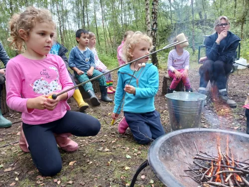 Children holding sticks with marshmallows on the fire at a forest school activity