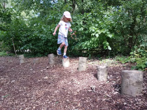 Child jumping on logs at forest school