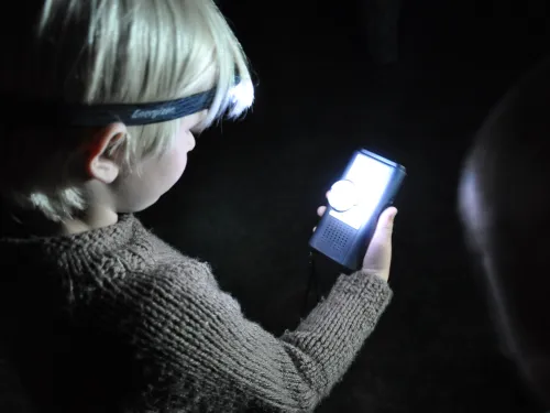 A child wearing a jumper and head torch looking at a bat detector