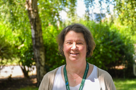 Jane Ibbotson, trustee, standing in front of trees and bushes.