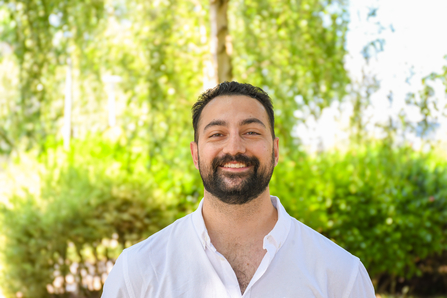 Kiran Rayner, trustee, standing in front of green trees and bushes.