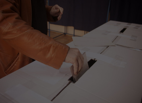 Person in a leather jacket putting a ballot paper into a box